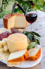 Vassoio con pecorino sardo, salsiccia secca di maiale, pane carasau e calice di vino rosso, gastronomia sarda, cibo italiano 