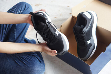 Close up hand holds and check quality and condition of new sneaker shoes from paper cardboard...