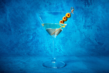 Martini. A glass of dirty martini cocktail with vermouth and olives, aperitif, on a blue background, side view - obrazy, fototapety, plakaty