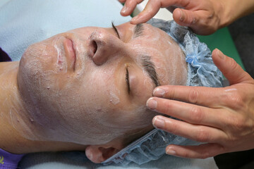 A cosmetologist applied a medicinal scrub cream for acne to a teenage boy.