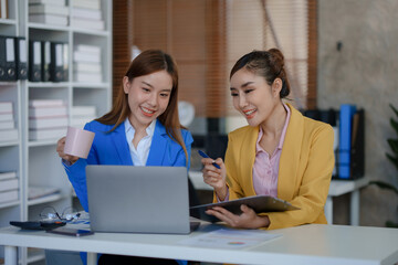 Two happy asian businesswoman talking and using a laptop computer in a meeting.