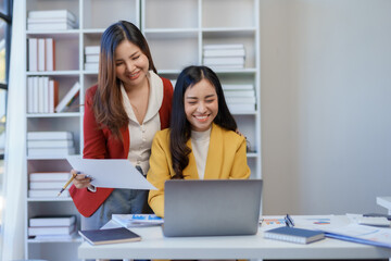 Two happy asian businesswoman talking and using a laptop computer in a meeting.