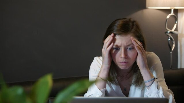A young professional business woman receiving bad news. The girl is working on a laptop computer and is sad and upset at losing