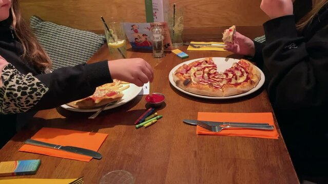 Children eating pizza and fries in a restaurant. A girl ids dipping a fry into tomato ketchup