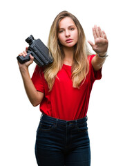 Young beautiful blonde woman filming using vintage camera over isolated background with open hand doing stop sign with serious and confident expression, defense gesture