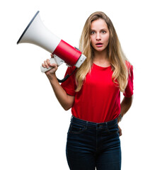 Young beautiful blonde woman yelling through megaphone over isolated background scared in shock with a surprise face, afraid and excited with fear expression