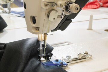 Close-up of sewing machine working with with thread inserted on the needle and fabric item of clothing. Workplace of seamstress. Sewing process in the phase of overstitching