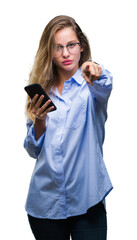 Young beautiful blonde business woman using smartphone over isolated background pointing with finger to the camera and to you, hand sign, positive and confident gesture from the front