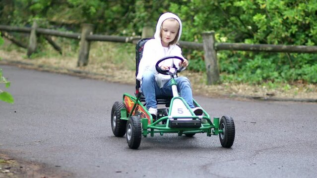 Preschooler girl driving pedal race car in amusement park with road surface marking and traffic lights