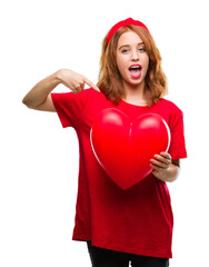 Young beautiful woman holding red heart in love over isolated background with surprise face pointing finger to himself