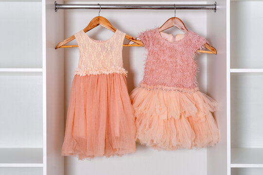 Elegant peach color dresses hanging on wooden racks in white wardrobe.
