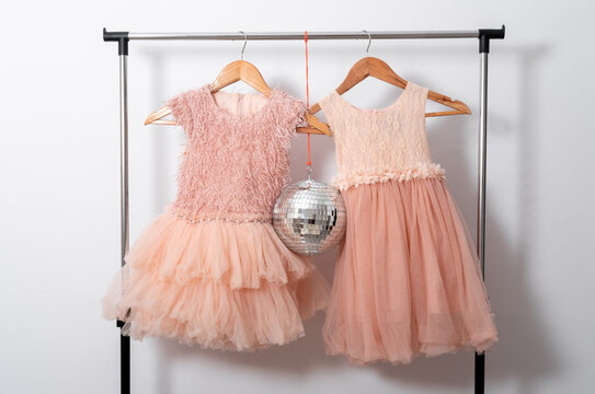 Cute dresses hang on hangers on clothes rail with disco ball on white wall background.