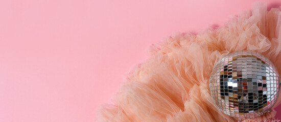 Top view flat lay fluffy tulle textile and disco ball on a pink background.