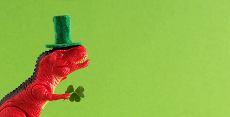 Red dinosaur in green hat holds leaf of clover. Wide banner. Copy space.