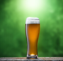 Beer in glass on wooden table with blurred green background.