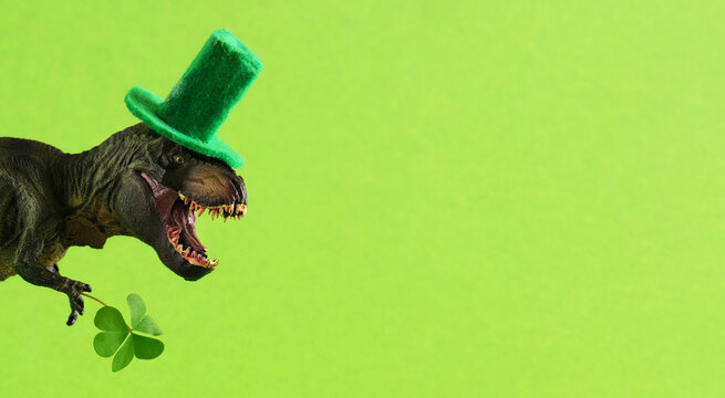 Green dinosaur in green hat holds leaf of clover. Wide banner. Copy space.
