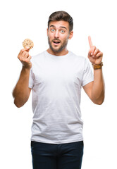 Young handsome man eating chocolate chips cookie over isolated background surprised with an idea or question pointing finger with happy face, number one