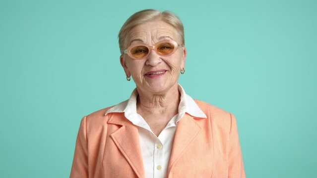 Happy female blonde of 60-70 years with deep wrinkles with short haircut wearing white shirt and orange jacket laughing heartily at camera. Flirting granny. High quality 4k footage