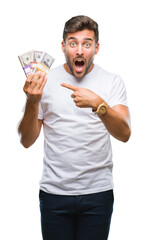 Young handsome man holding stack of dollars over isolated background very happy pointing with hand and finger