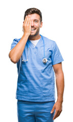 Young handsome doctor surgeon man over isolated background covering one eye with hand with confident smile on face and surprise emotion.