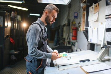 Print house worker controlling printing process quality and checking colors with magnifying glass