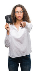 Fototapeta premium Young hispanic woman holding passport of Canada pointing with finger to the camera and to you, hand sign, positive and confident gesture from the front