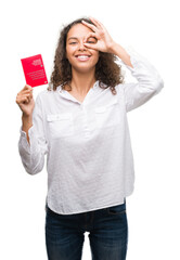 Young hispanic woman holding passport of Switzerland with happy face smiling doing ok sign with hand on eye looking through fingers