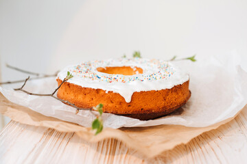 Round Easter cupcake decorated with white protein cream and colorful sprinkles on a white background with young tree branches. Front view