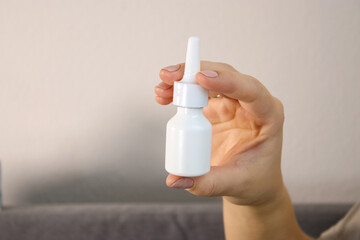 Close up of sick woman holing white nose spray bottle, blurry background 