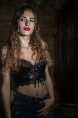 pretty woman in black top and jeans stands near an old stone wall and rustic wooden door