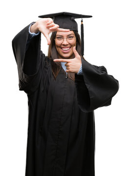 Young hispanic woman wearing graduated cap and uniform smiling making frame with hands and fingers with happy face. Creativity and photography concept.