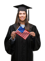 Young hispanic woman wearing graduated uniform holding flag of america with a happy face standing and smiling with a confident smile showing teeth