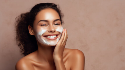 Beautiful young woman applying facial mask on her face. Skin care and treatment, spa, natural beauty and cosmetology concept, over beige background with copy space - obrazy, fototapety, plakaty