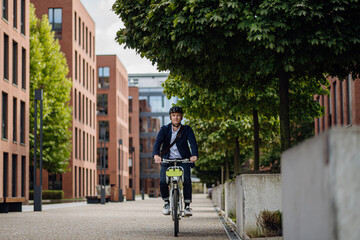 Handsome middle-aged man commuting through the city by bike, riding bicycle. Male city commuter traveling from work by bike after a long workday.