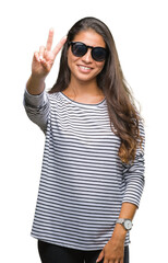 Young beautiful arab woman wearing sunglasses over isolated background smiling with happy face winking at the camera doing victory sign. Number two.