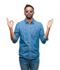 Adult hispanic man wearing sunglasses over isolated background relax and smiling with eyes closed doing meditation gesture with fingers. Yoga concept.
