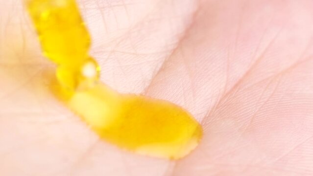 Close up of yellow serum gel or oil falling on the skin. Macro shot of transparent orange serum gel in pipette falling on the palm. Health care cosmetics.