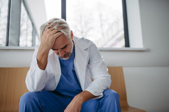 Low angle shot of frustrated, exhausted doctor sitting in hospital corridor. Concept of burnout syndrome among doctors.