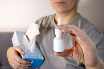 Close up of sick woman holing white nose spray bottle, blurry background 