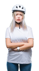 Young blonde woman wearing cyclist security helmet over isolated background skeptic and nervous, disapproving expression on face with crossed arms. Negative person.