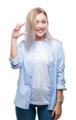 Young blonde woman over isolated background smiling and confident gesturing with hand doing size sign with fingers while looking and the camera. Measure concept.