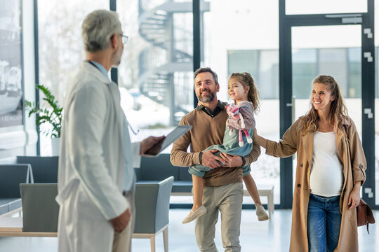 Girl patient looking forward to her doctor and examination in a modern clinic. Girl arriving in hospital with her parents. Emotional support during medical examination. - Powered by Adobe