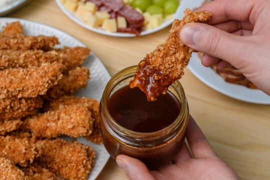Panierowany w panko kurczaka zanurzany w sosie bbq leży na stole wśr&oacute;d innych przekąsek 