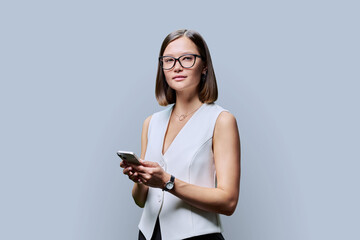 Young business woman in glasses using smartphone on gray background
