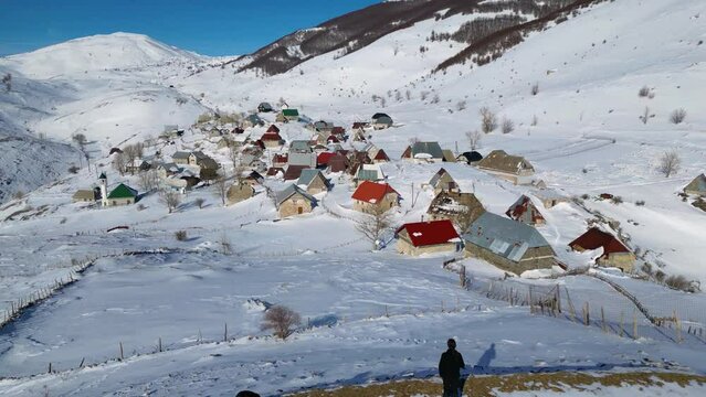 Aerial drone view of a solo hiker admiring a mountain village during winter. Snow white landscape and mountaineer lifestyle.