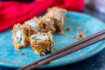 Vegetable sushi roll topped with spicy mayo, teriyaki sauce and fried onions on a turquoise plate with chopsticks