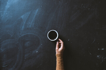 Woman hand holding ceramic coffee mug on blackboard