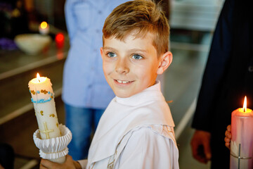 Little kid boy receiving his first holy communion. Happy child holding Christening candle....