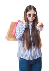 Young Chinese woman over isolated background holding shopping bags on sales with angry face, negative sign showing dislike with thumbs down, rejection concept