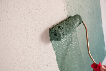 Repairman painting white wall in apartment green using roller, closeup